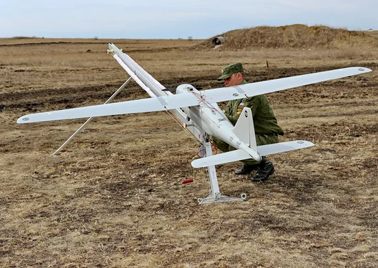 Військовий у камуфляжі перевіряє білий розвідувальний безпілотник на сухому полі